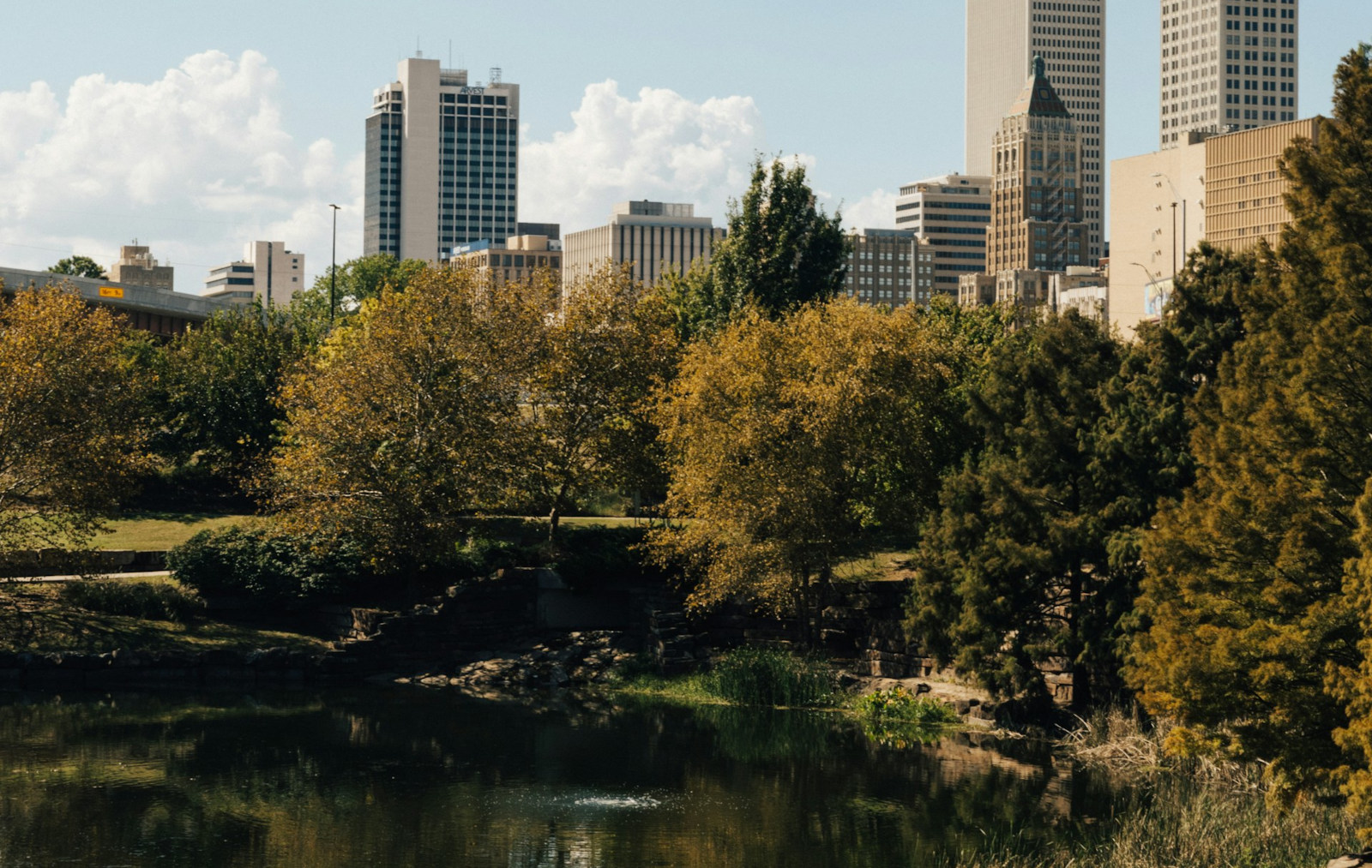 This daytime view of the Tulsa skyline showcases the city's harmonious blend of modern urban development and serene natural spaces. This specific perspective is captured from Centennial Park, a 13-acre destination known for offering one of the best 